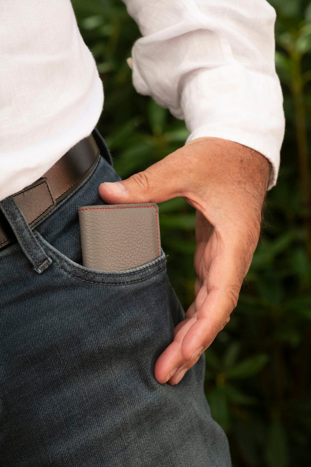 Porte-cartes artisanal Le10Colonne en cuir de chèvre gris et coutures rouges présenté en situation lifestyle